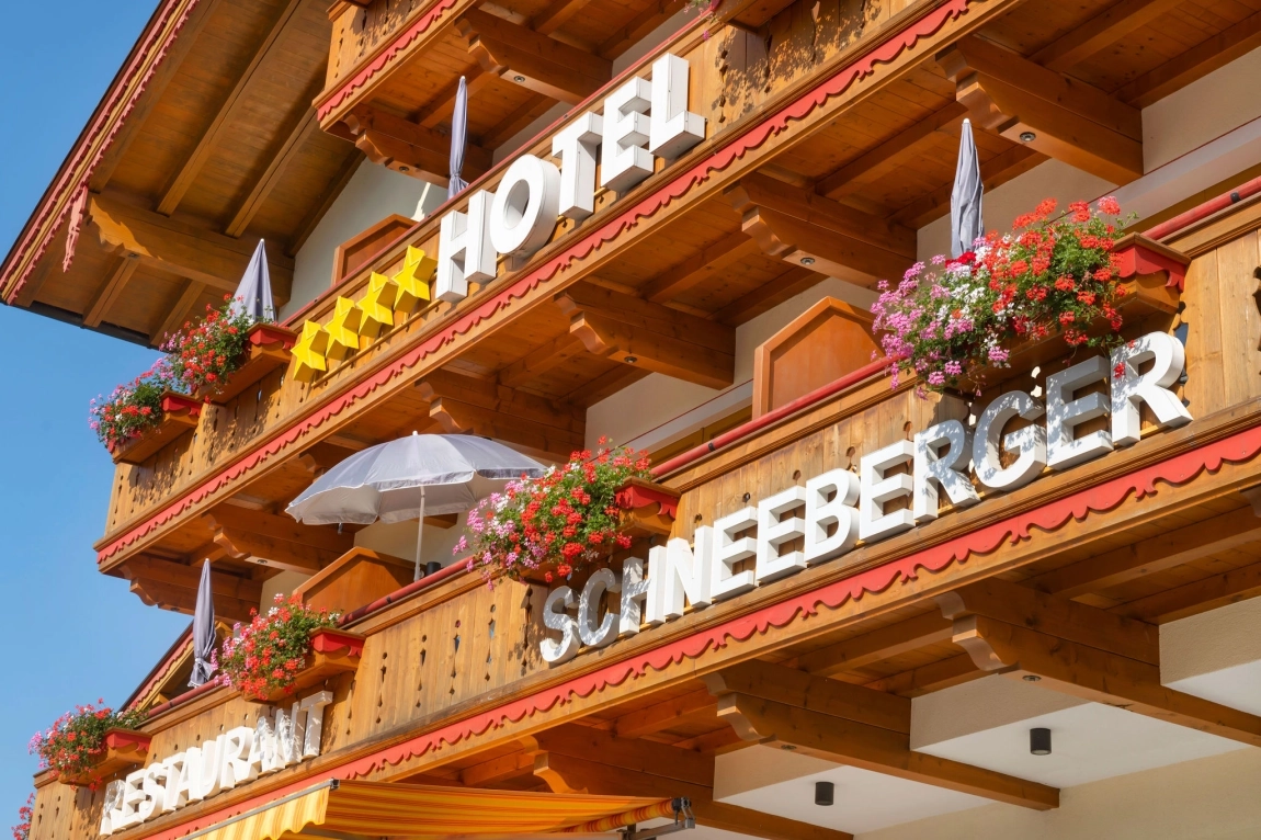 Fassade des Hotels Schneeberger mit Holzverkleidung, großen Buchstaben, Balkonen und Blumenkästen.