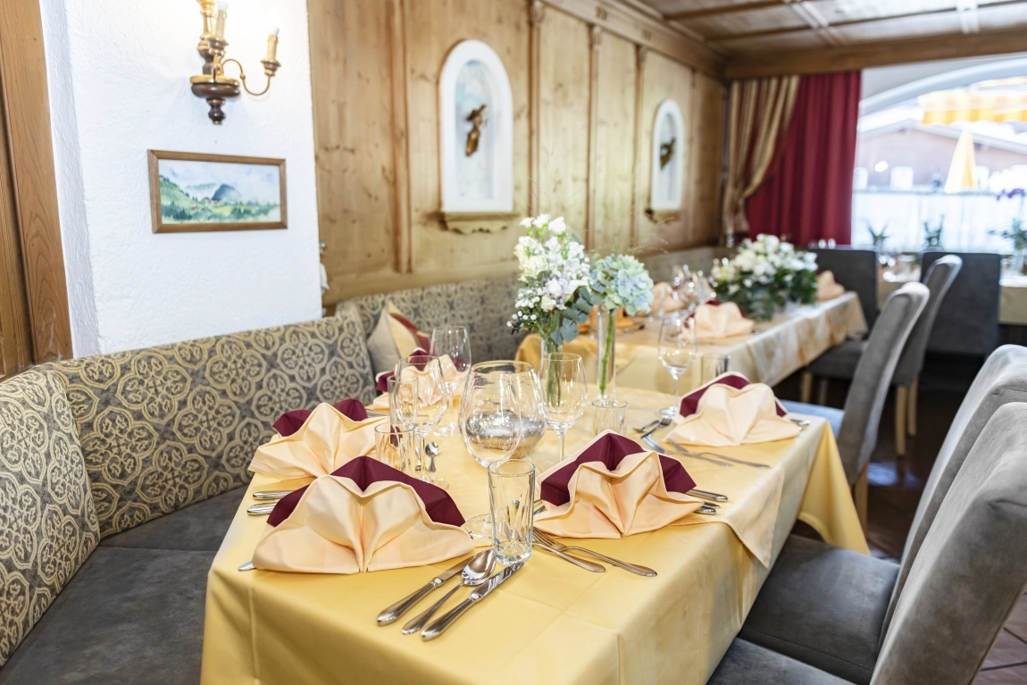 Festlich gedeckter Tisch im Restaurant mit Servietten, Gläsern, Blumendeko, Polsterbank und Holzverkleidung.