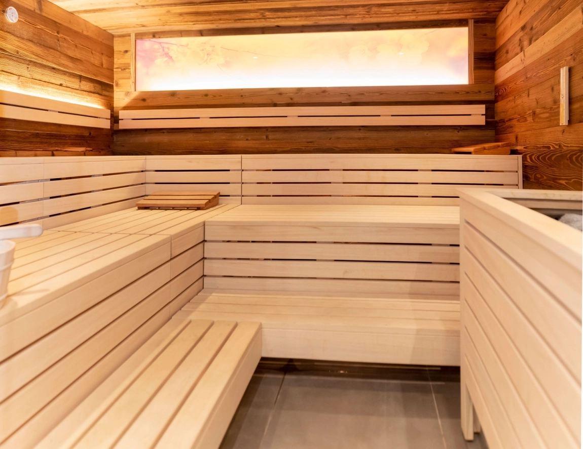 Eine Sauna mit hellen Holzpanelen, einem Fenster mit weichem Licht und Holzbänken für Entspannung.