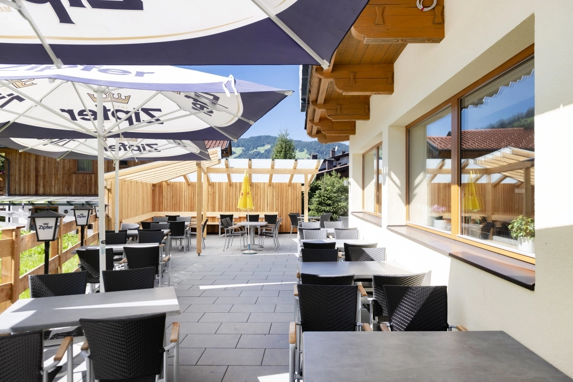 Barrierefreie Terrasse mit Tischen, Stühlen und großen Sonnenschirmen neben dem Gebäude im Außenbereich.