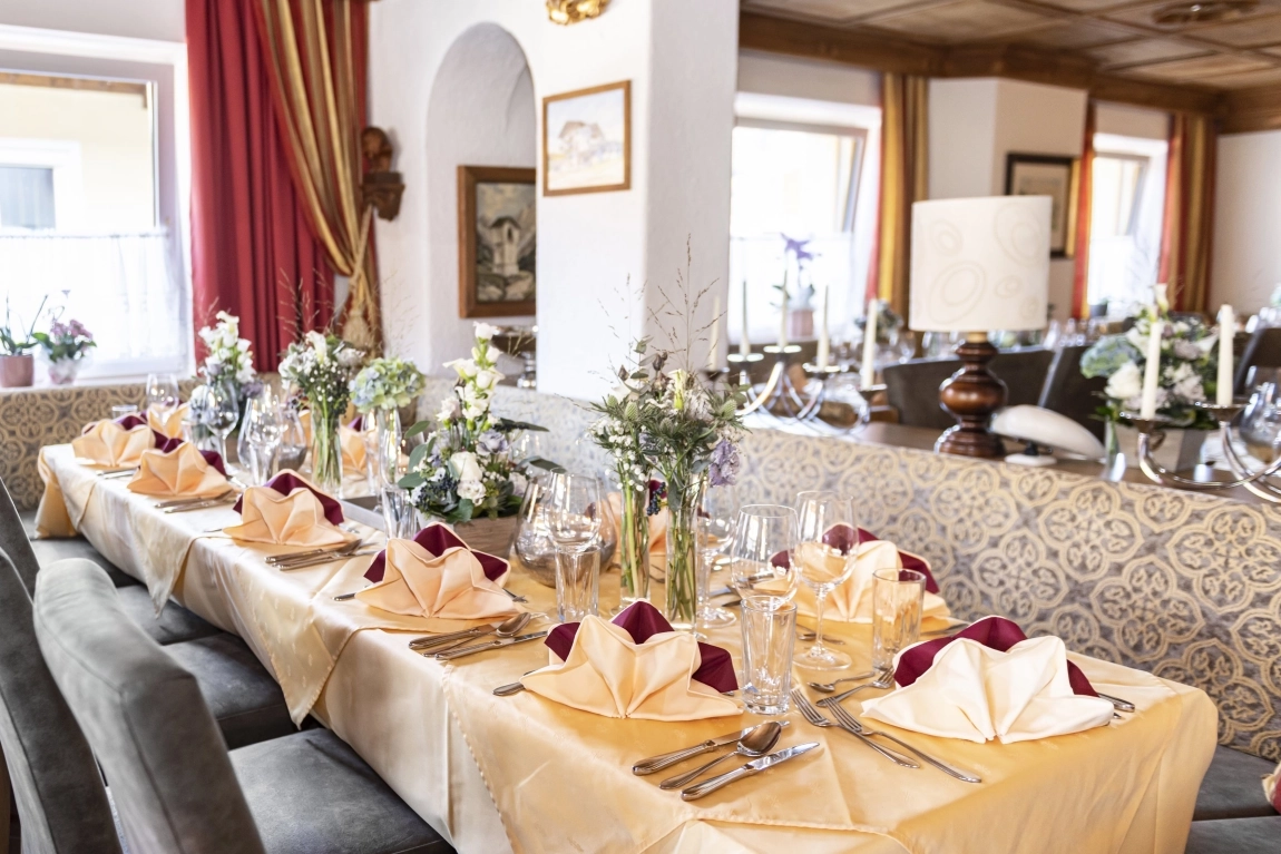 Lang gedeckter Tisch im Restaurant mit Servietten, Besteck, Gläsern, Blumen und gepolsterten Stühlen.
