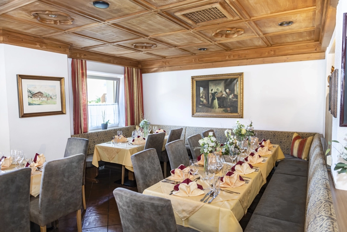 Restaurantbereich mit Holzdecke, gedeckten Tischen, Polsterbänken, Stühlen, Blumendeko und Wandgemälden.