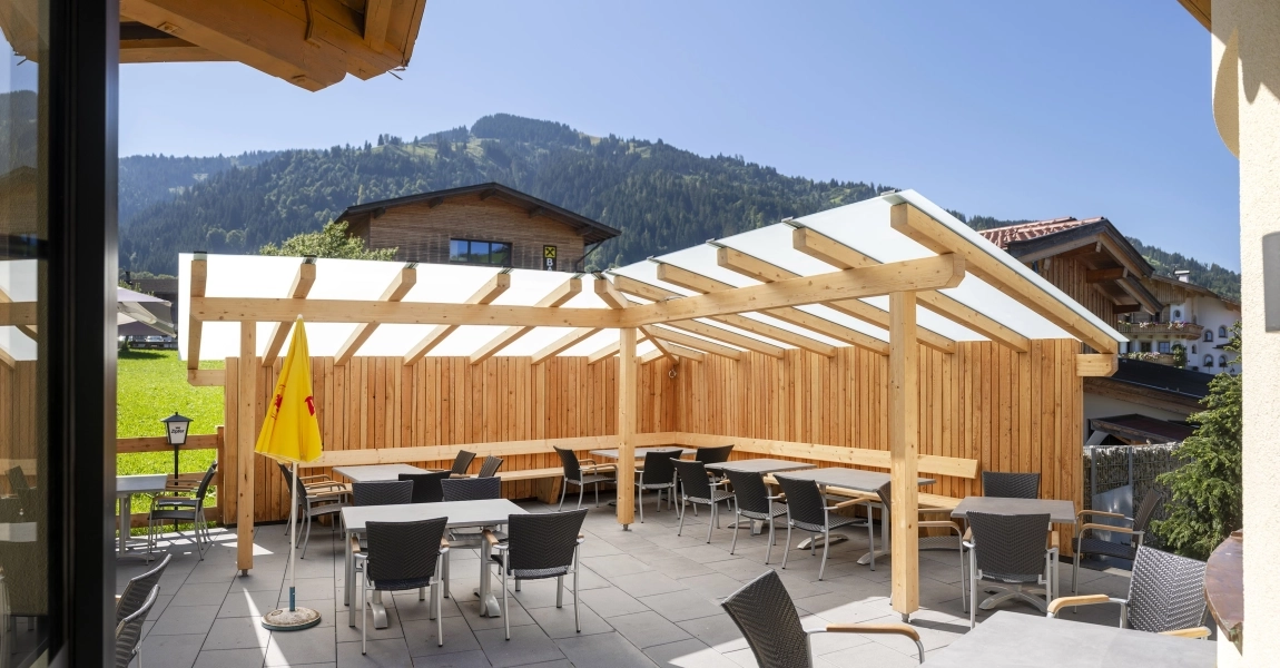 Überdachte Sitzterrasse mit Tischen, Stühlen und Bergblick, barrierefrei erreichbar im Außenbereich des Hotels.