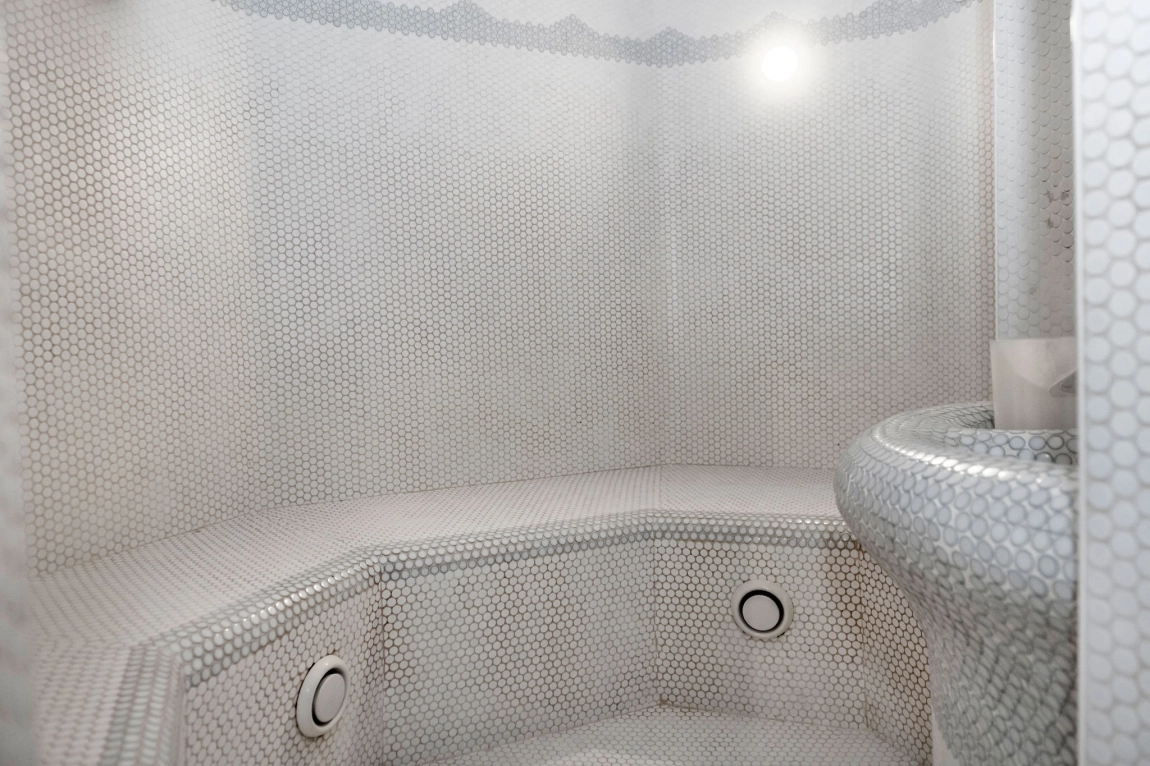 Heller Raum mit Mosaikfliesen, gewölbter Sitzbank und Dampfauslass – ein barrierefreier Bereich zum Entspannen im Dampfbad.