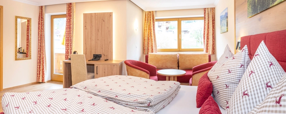 Geräumiges, helles Zimmer mit Doppelbett, Sofa, zwei Sesseln, Tisch und großen Fenstern mit Blick ins Grüne.