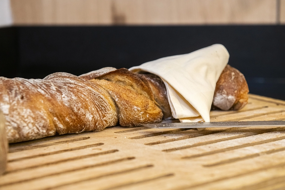 Frisches Brot auf Holzbrett mit Schneidemesser und Stoffserviette, bereit zur Selbstbedienung am Frühstücksbuffet.