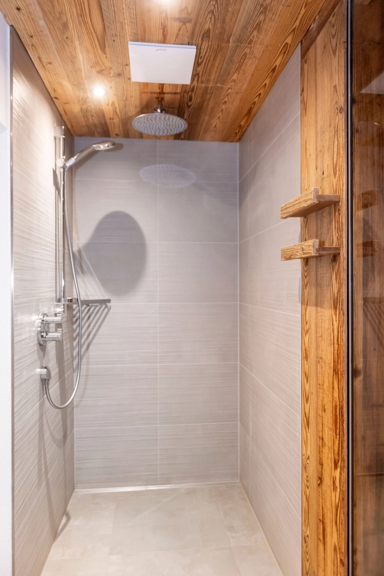 Eine moderne Duschkabine mit Fliesenwänden, Holzregal an der Wand und einer Regendusche an der Decke.
