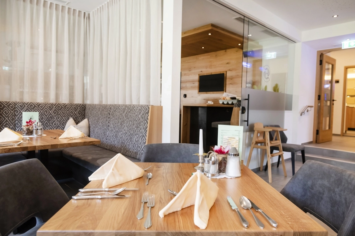 Tisch im Hotelrestaurant mit Besteck und Servietten, Sitzbank, Vorhängen und angrenzendem barrierefreiem Zugang.