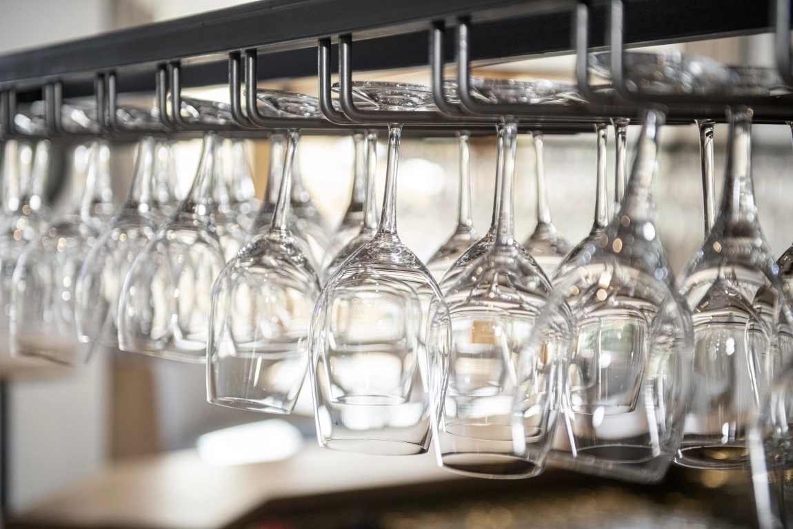 Reihe sauber aufgehängter Weingläser über einer Bar – elegantes Detail aus dem Innenraum der dorfStub’n.