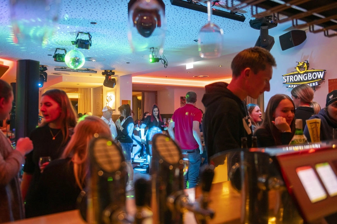 Gäste feiern am Abend in der Hotelbar mit Musik, Tanz, Lichteffekten und Blick über die Theke.