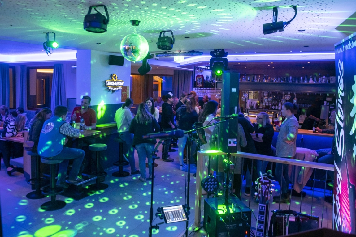 Stimmungsvolle Bar mit Gästen, Tanzfläche, Discokugel, Lichtspots und Livemusik-Ausrüstung am Abend.