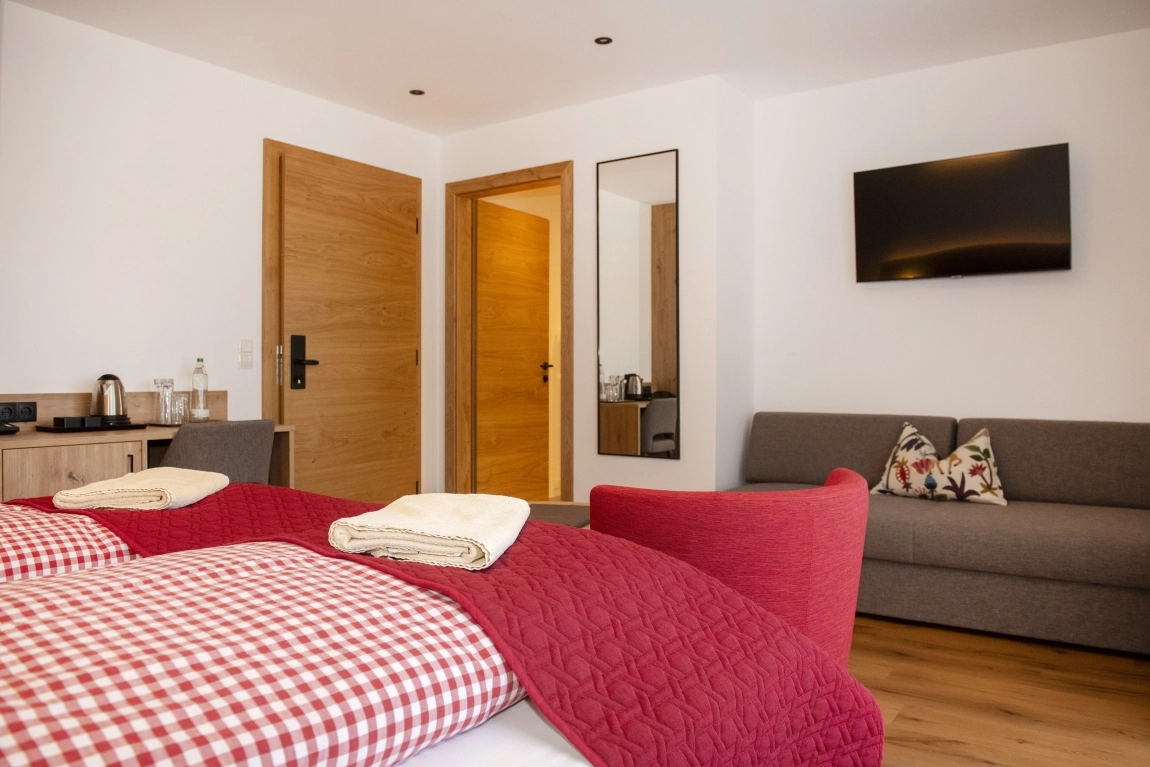 Modernes Zimmer mit Sofa, roter Sitzgelegenheit, Spiegel, TV, Holzfußboden und Wasserkocher auf Sideboard, helle und klare Einrichtung.