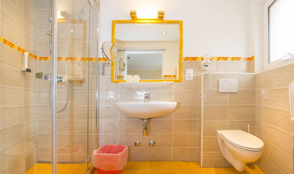 Modernes, barrierearmes Bad mit bodengleicher Dusche, kontrastreichem WC, hellem Spiegellicht und gut erkennbarem Boden.