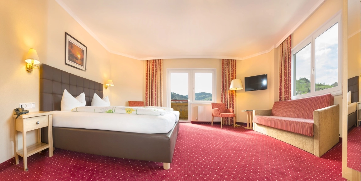 Helles Hotelzimmer mit Kontrasten: roter Teppich, dunkles Bett, helle Wände, viel Tageslicht, klare Wege und große Fenster.