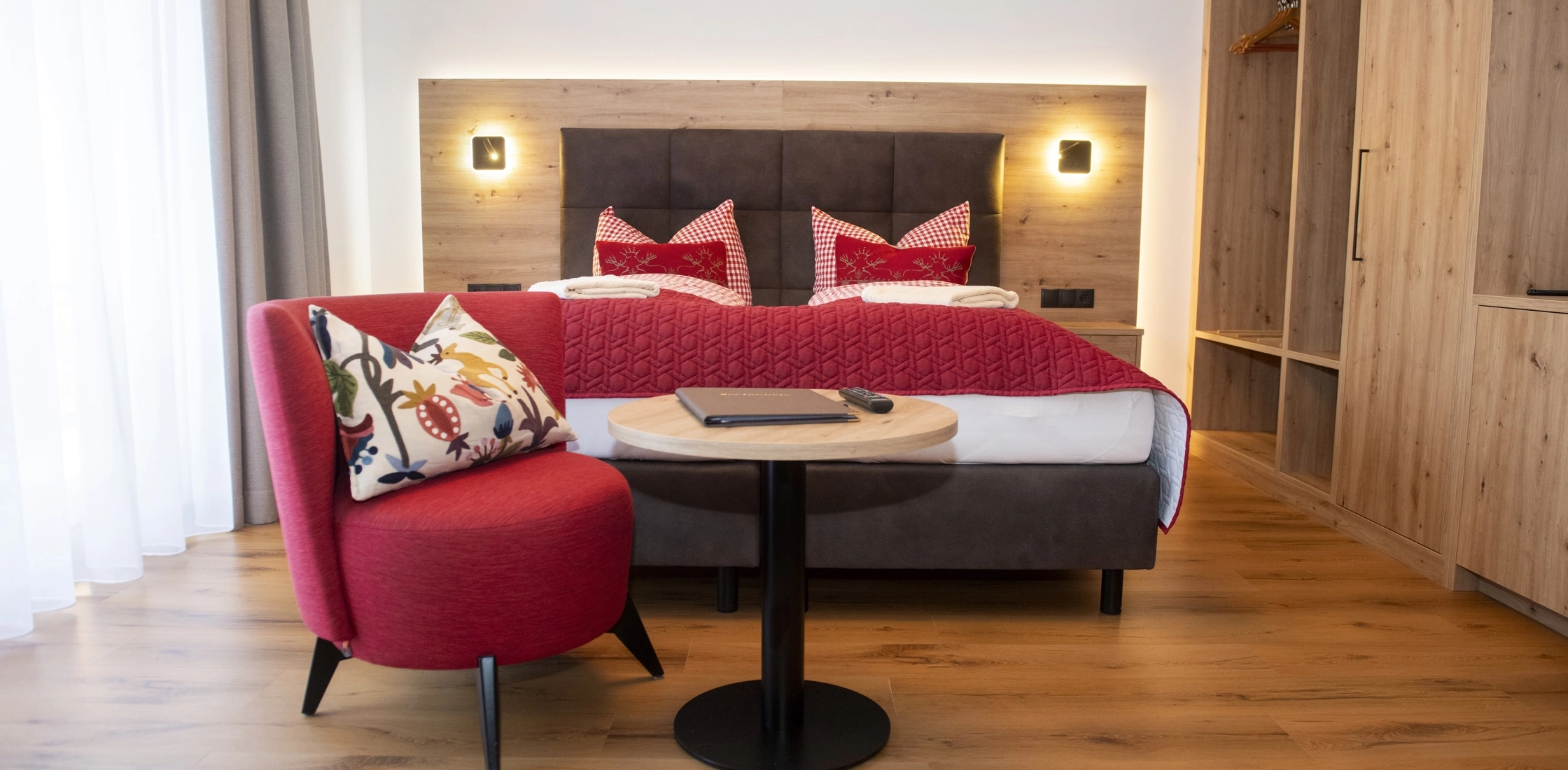 Modernes Zimmer mit kontrastreicher Einrichtung: roter Sessel, dunkler Tisch, gut ausgeleuchtetes Bett mit klaren Linien.