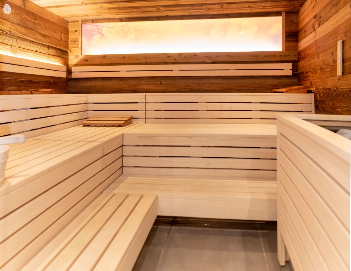 Eine Sauna mit hellen Holzpanelen, einem Fenster mit weichem Licht und Holzbänken für Entspannung.