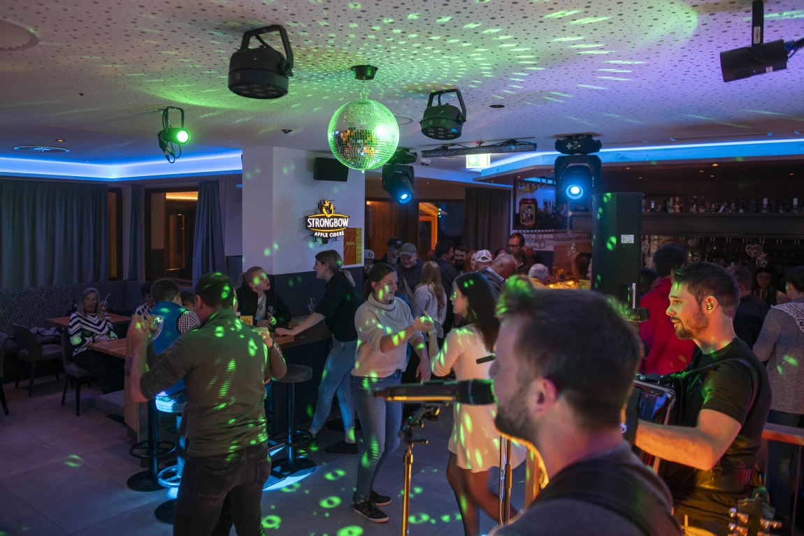 Abendveranstaltung mit Livemusik, Tanzenden, Discokugel und Lichteffekten in der Bar des Hotels.