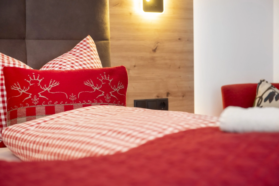 Detailansicht eines Hotelbetts mit kariertem Bettbezug, Zierkissen und modernem Holzwand-Element.