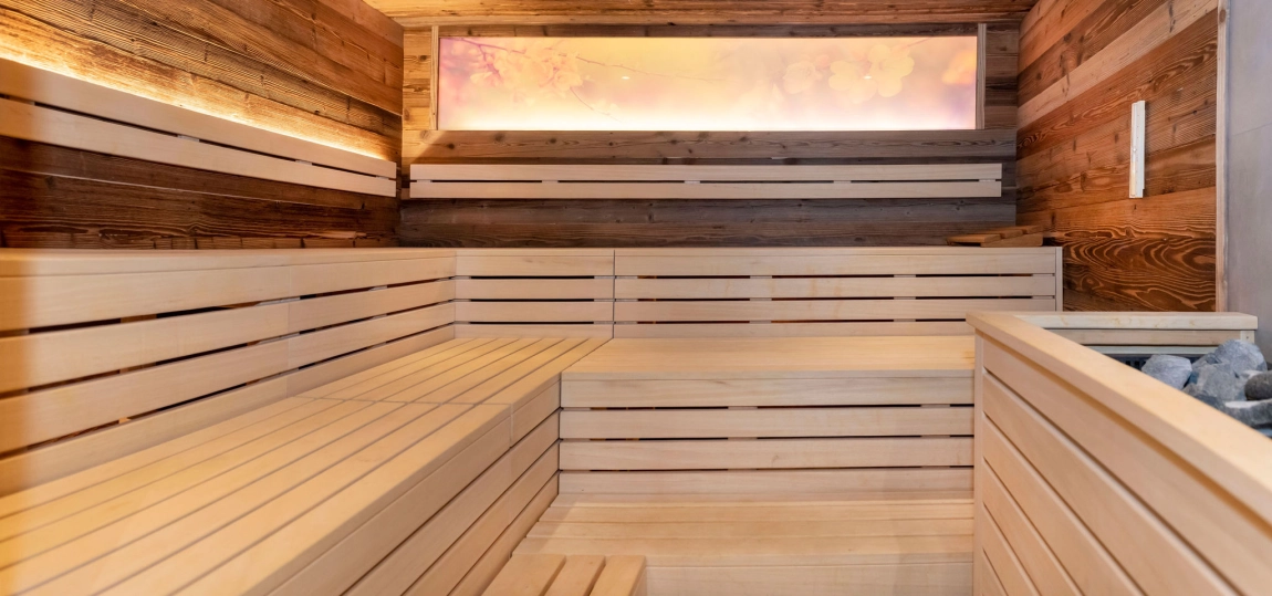 Innenansicht einer Sauna mit breiten Holzsitzflächen, mehreren Stufen und sanfter Beleuchtung an Wand und Decke.