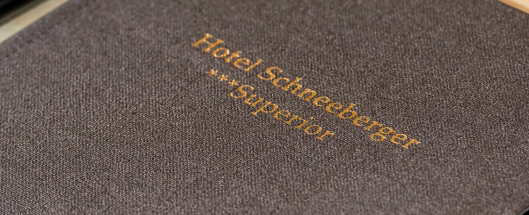 Detailaufnahme einer Mappe mit der Aufschrift ‚Hotel Schneeberger *Superior‘ in geprägter Schrift.