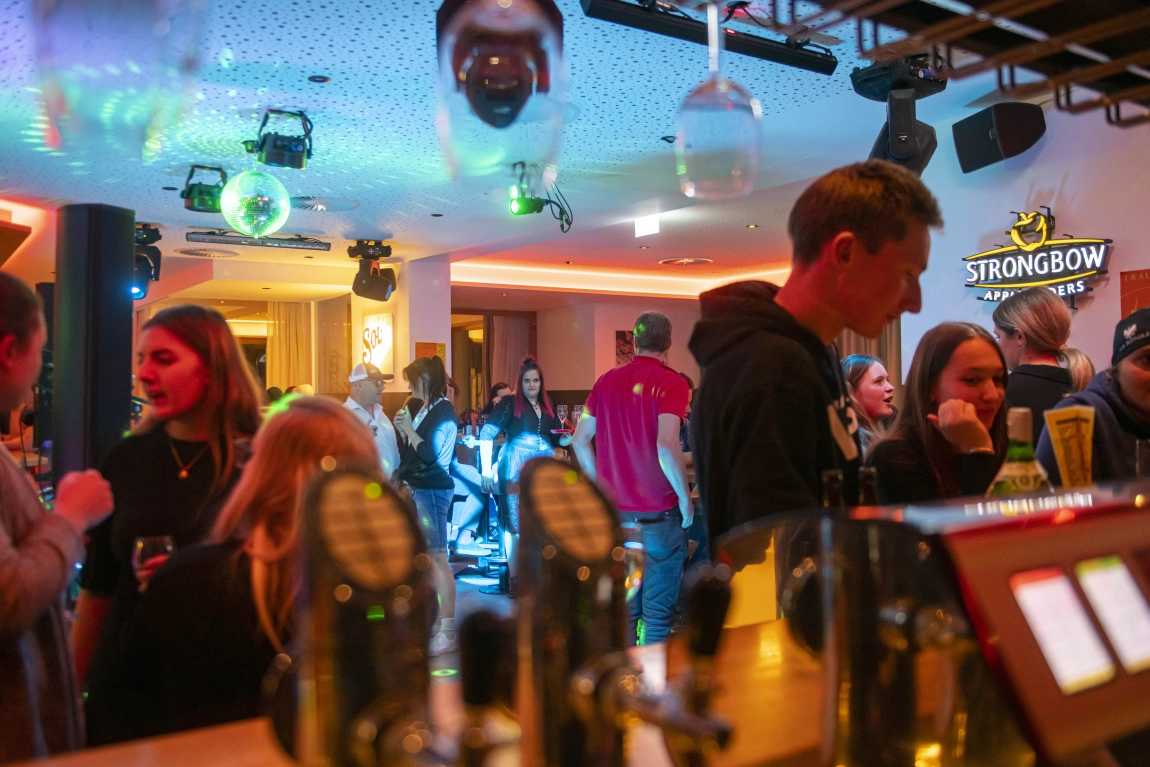 Gäste feiern am Abend in der Hotelbar mit Musik, Tanz, Lichteffekten und Blick über die Theke.
