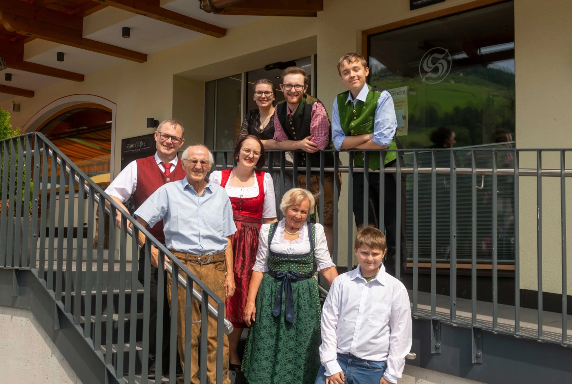 Die Betreiberfamilie des Hotels Schneeberger in Tracht stehend auf der Eingangstreppe vor dem Hotel.