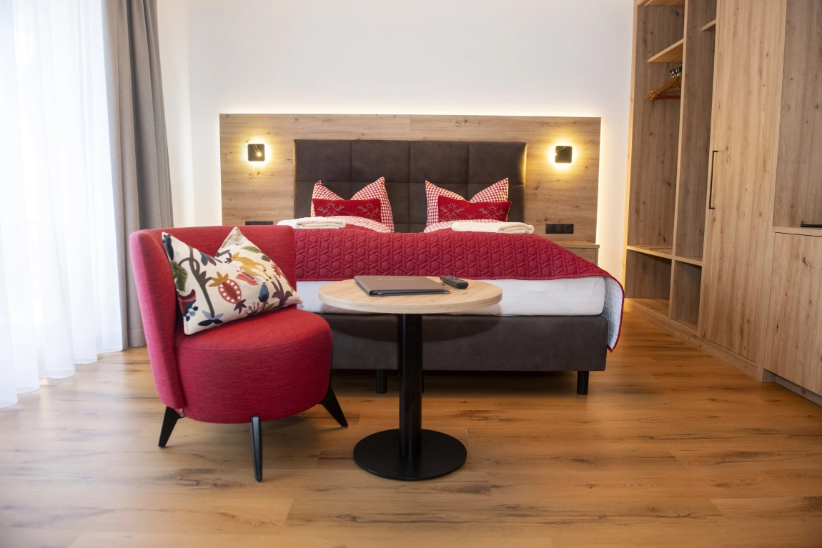 Modern eingerichtetes Hotelzimmer mit Doppelbett, Sessel, Tisch, Kleiderschrank und viel Tageslicht.